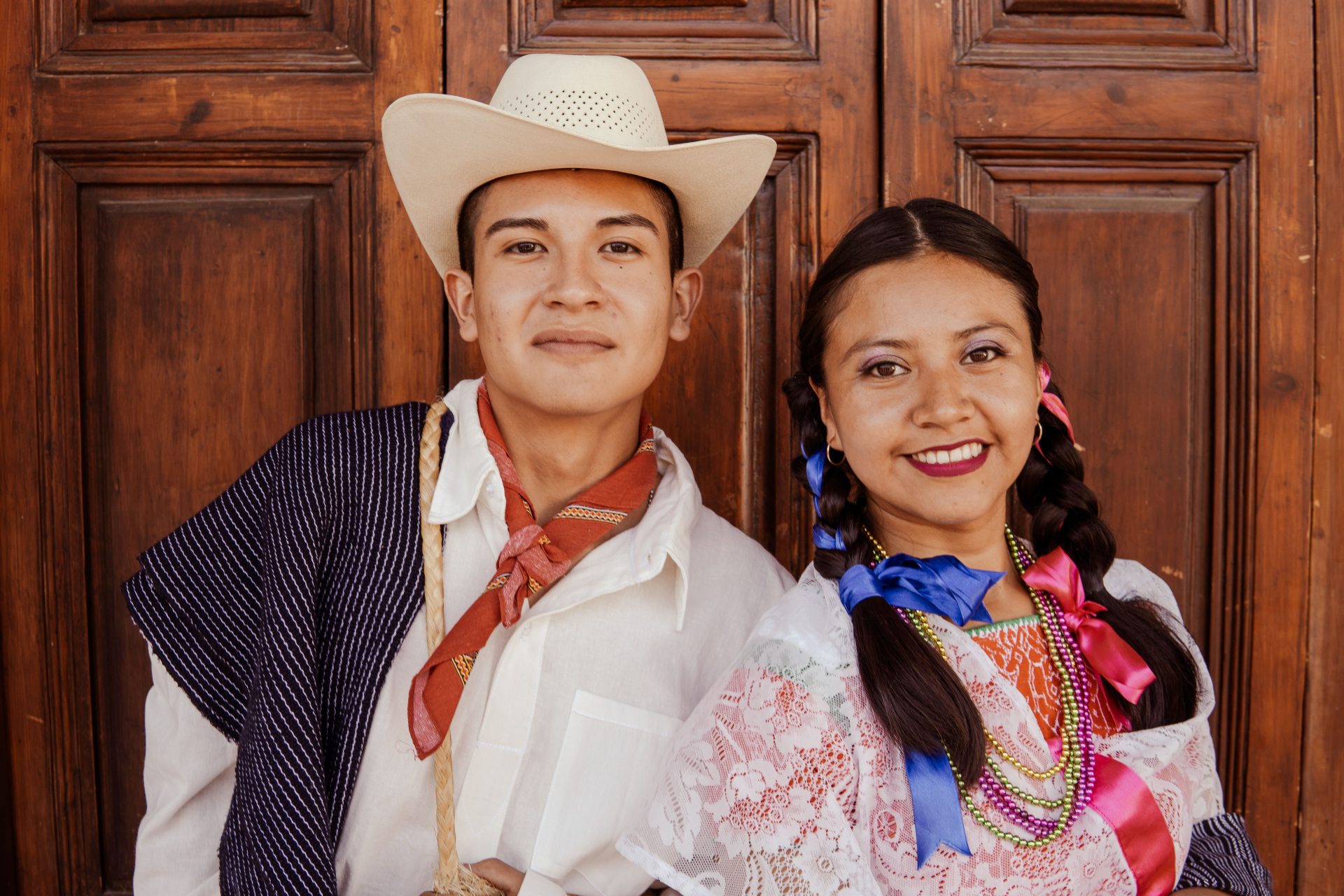 A Mexican couple dressed in vibrant traditional attire, smiling outdoors.