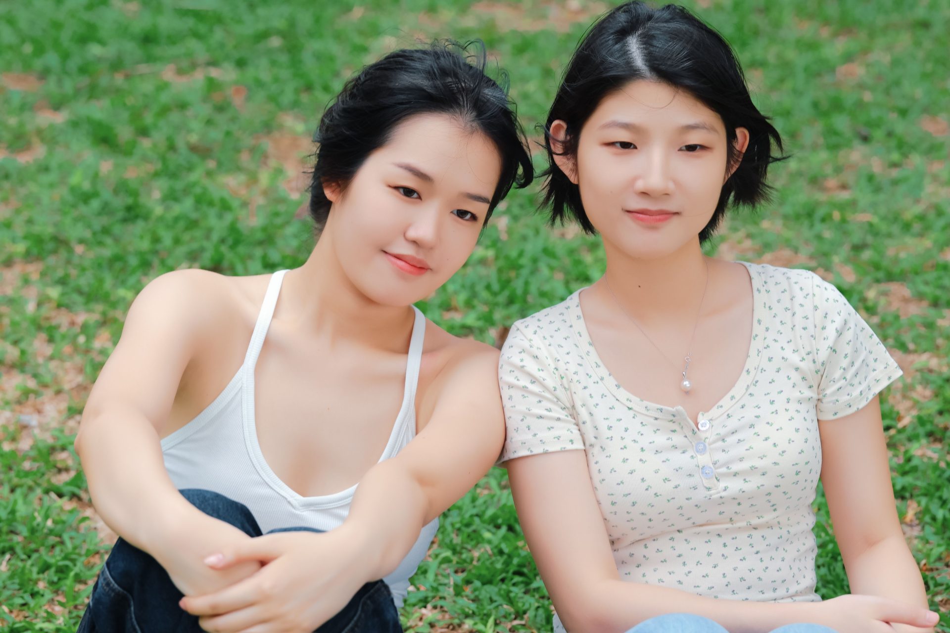 Two young women sitting on grass enjoying a sunny day outdoors.
