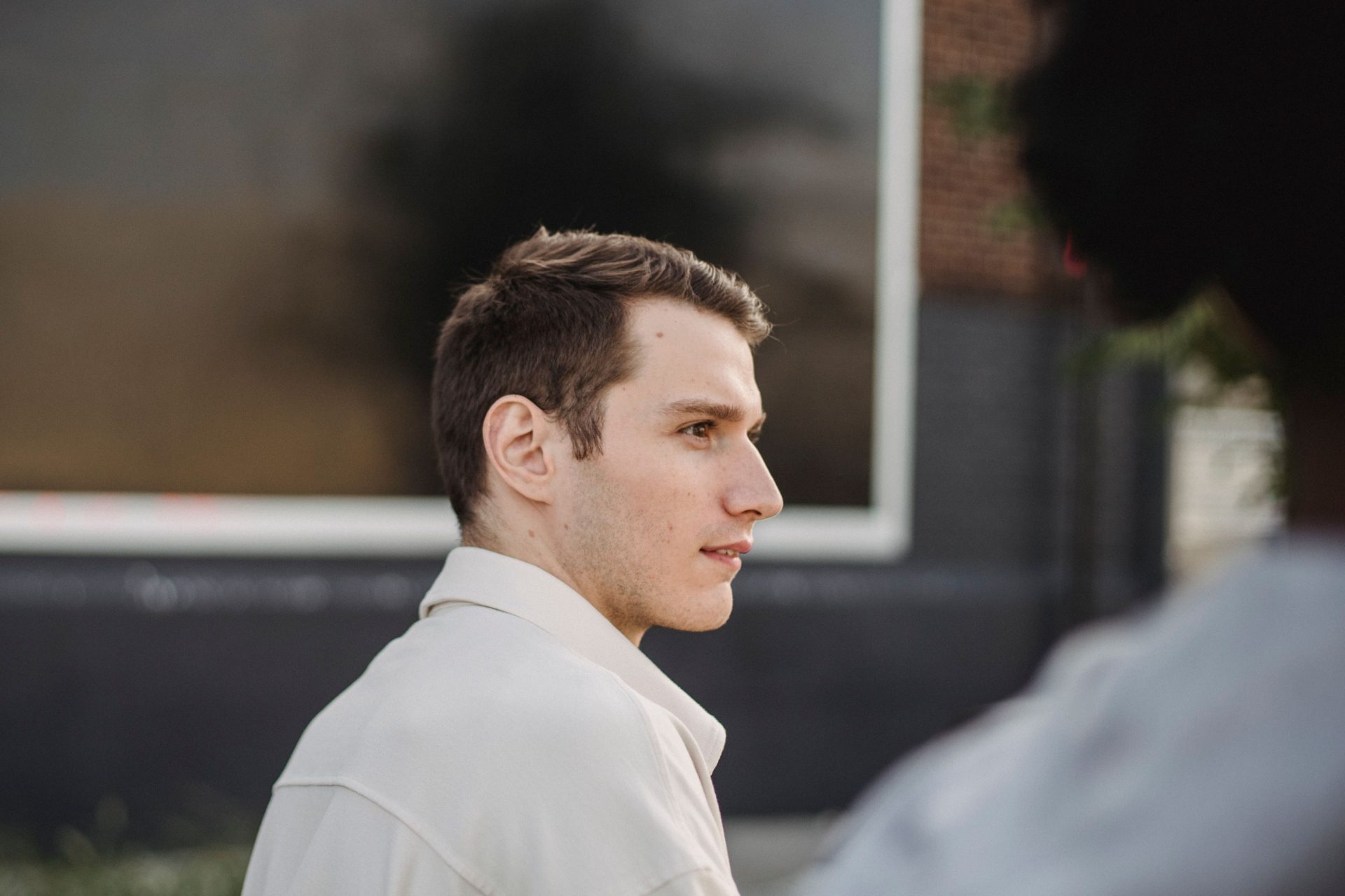 Side view of concentrated young male resting on city street and looking away thoughtfully on sunny day
