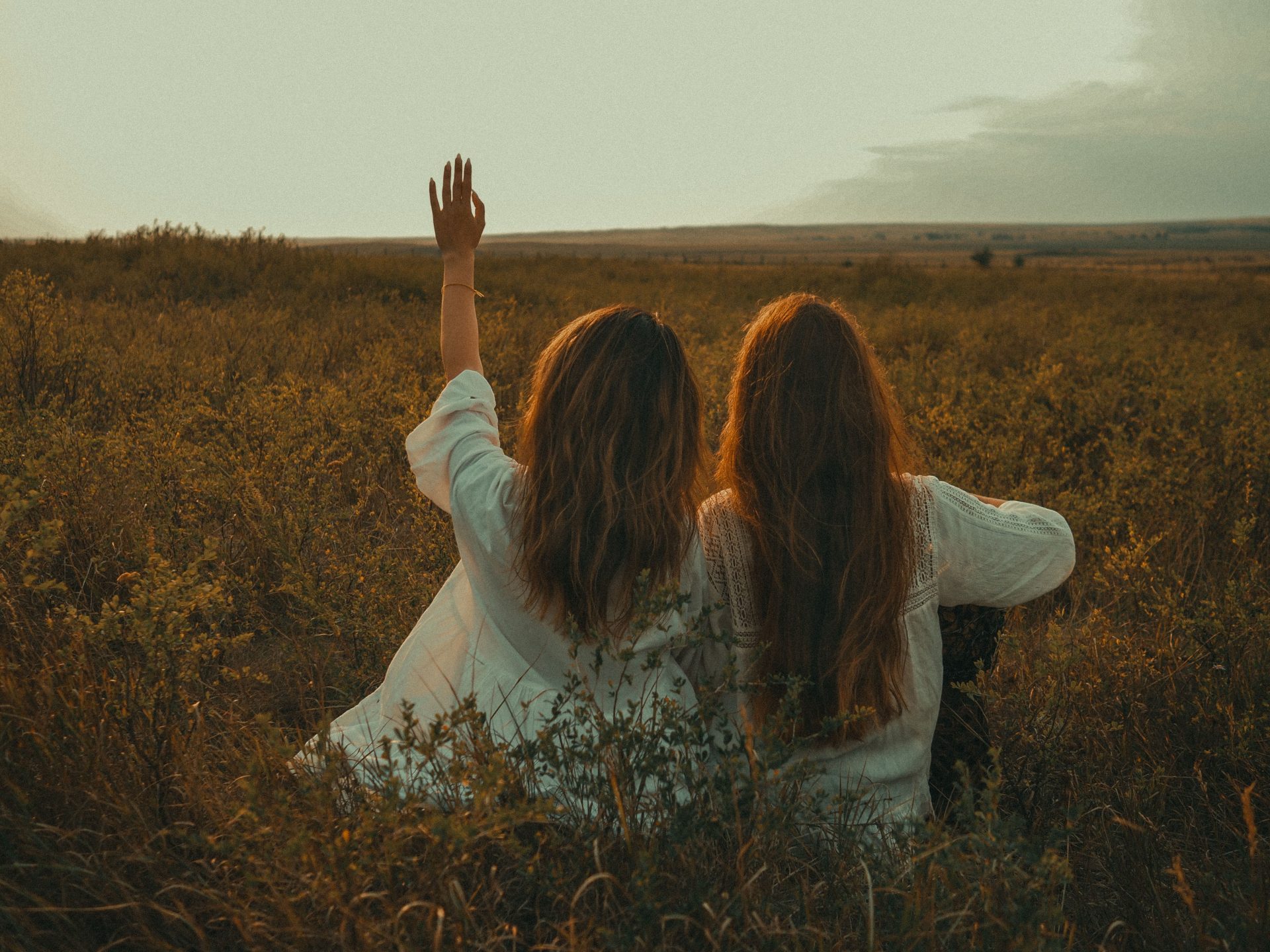 Two women in white dresses enjoying nature in a tranquil field, back view and boho style.